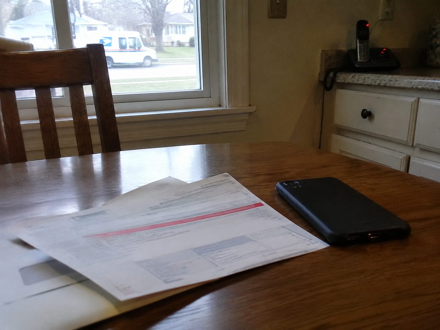 a past-due bill on a kitchen table with a phone turned face-down beside it